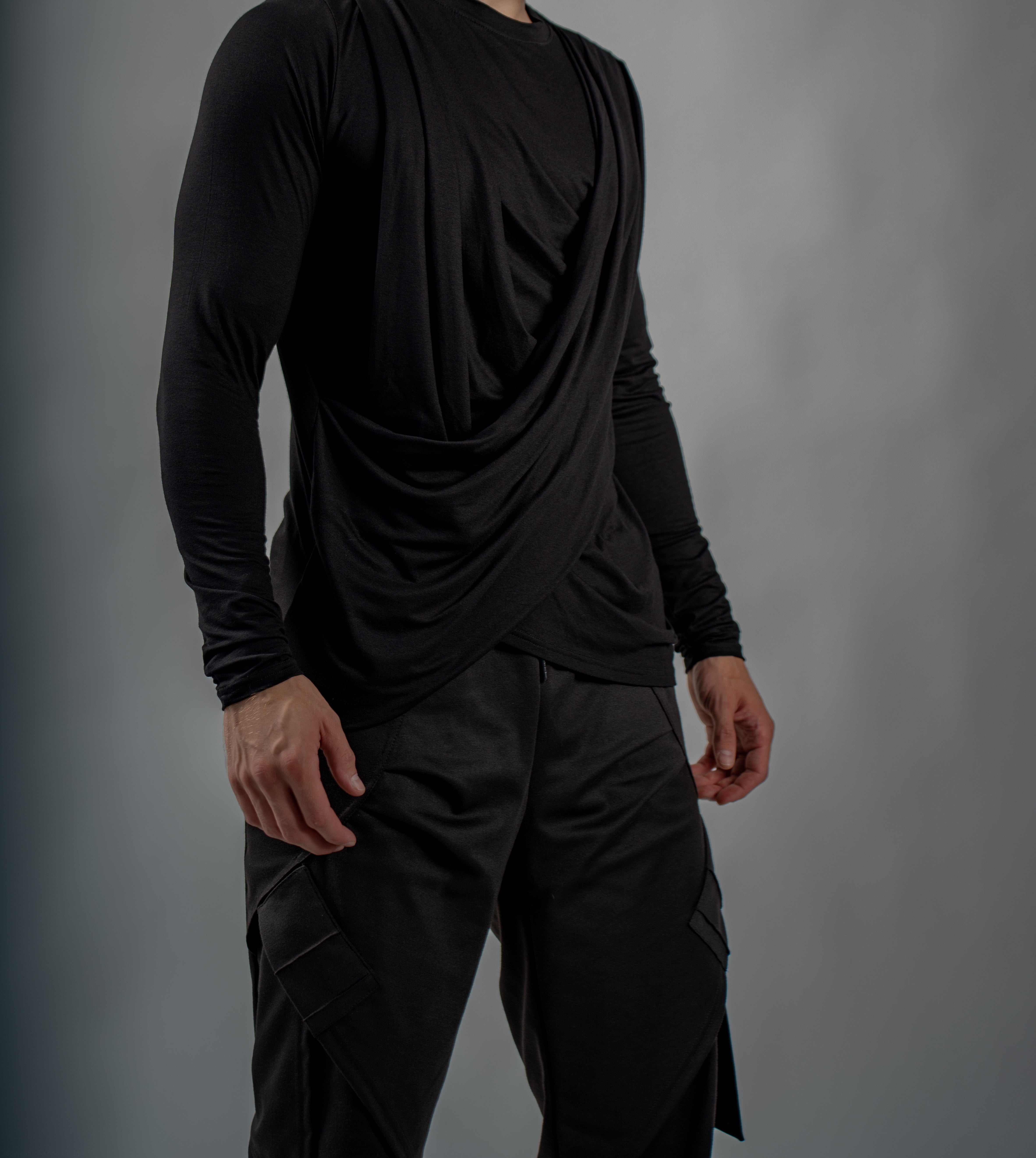 Person wearing a black long-sleeve top and black darkwear style pants against a gray background