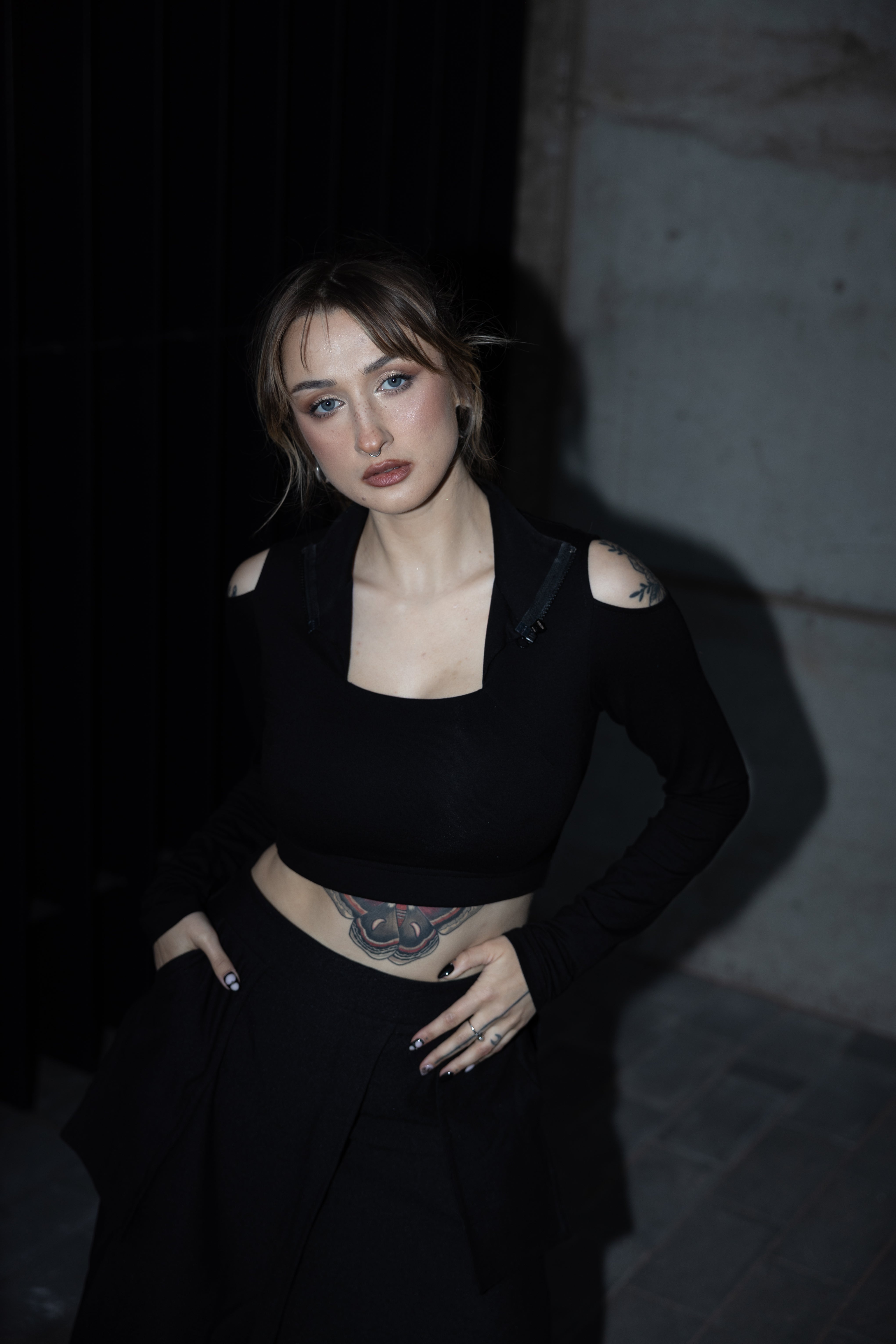 Woman wearing a black outfit with a tattoo on her waist against a dark background