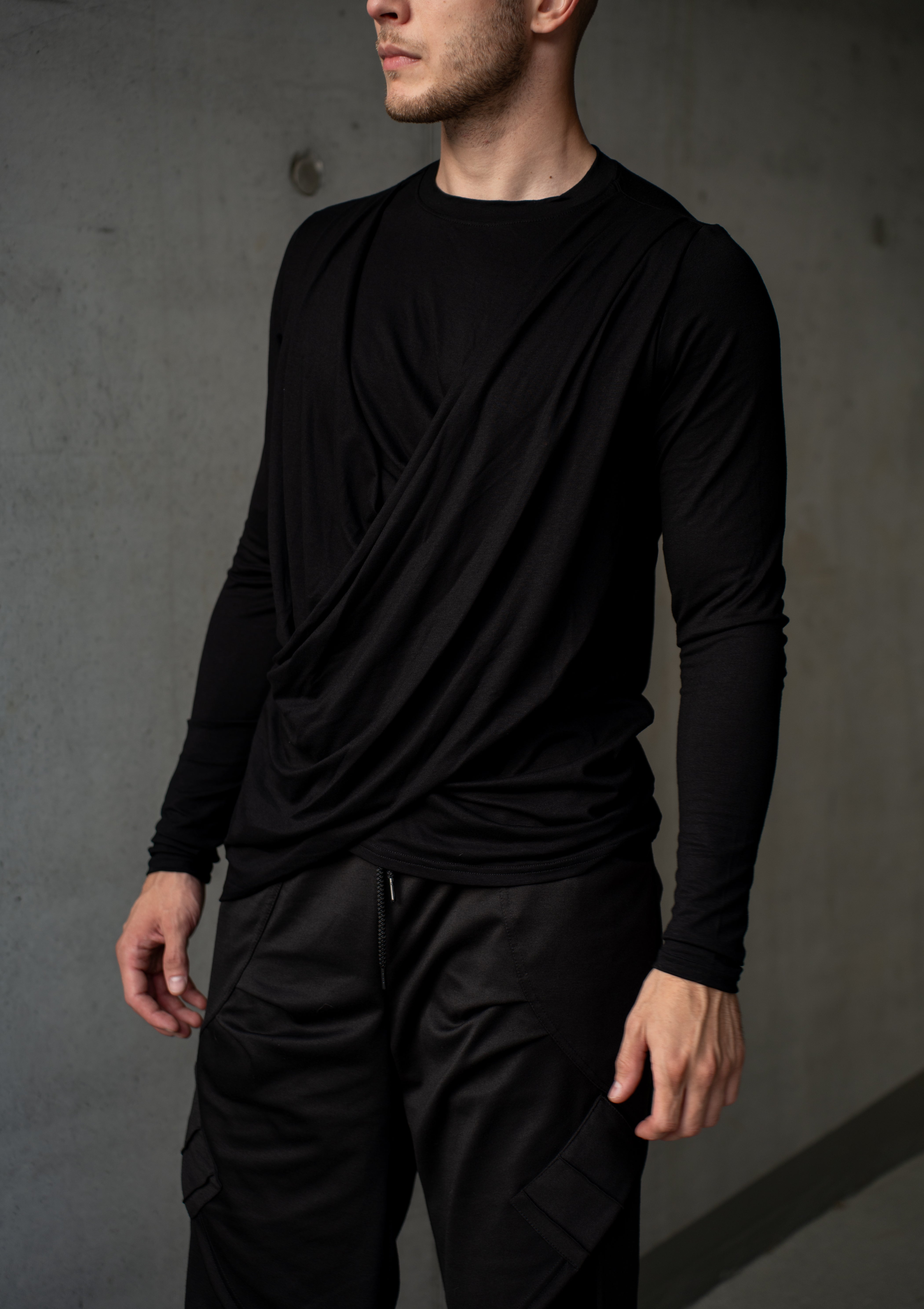 Person wearing a black long-sleeve top and techwear cargo pants against a gray background