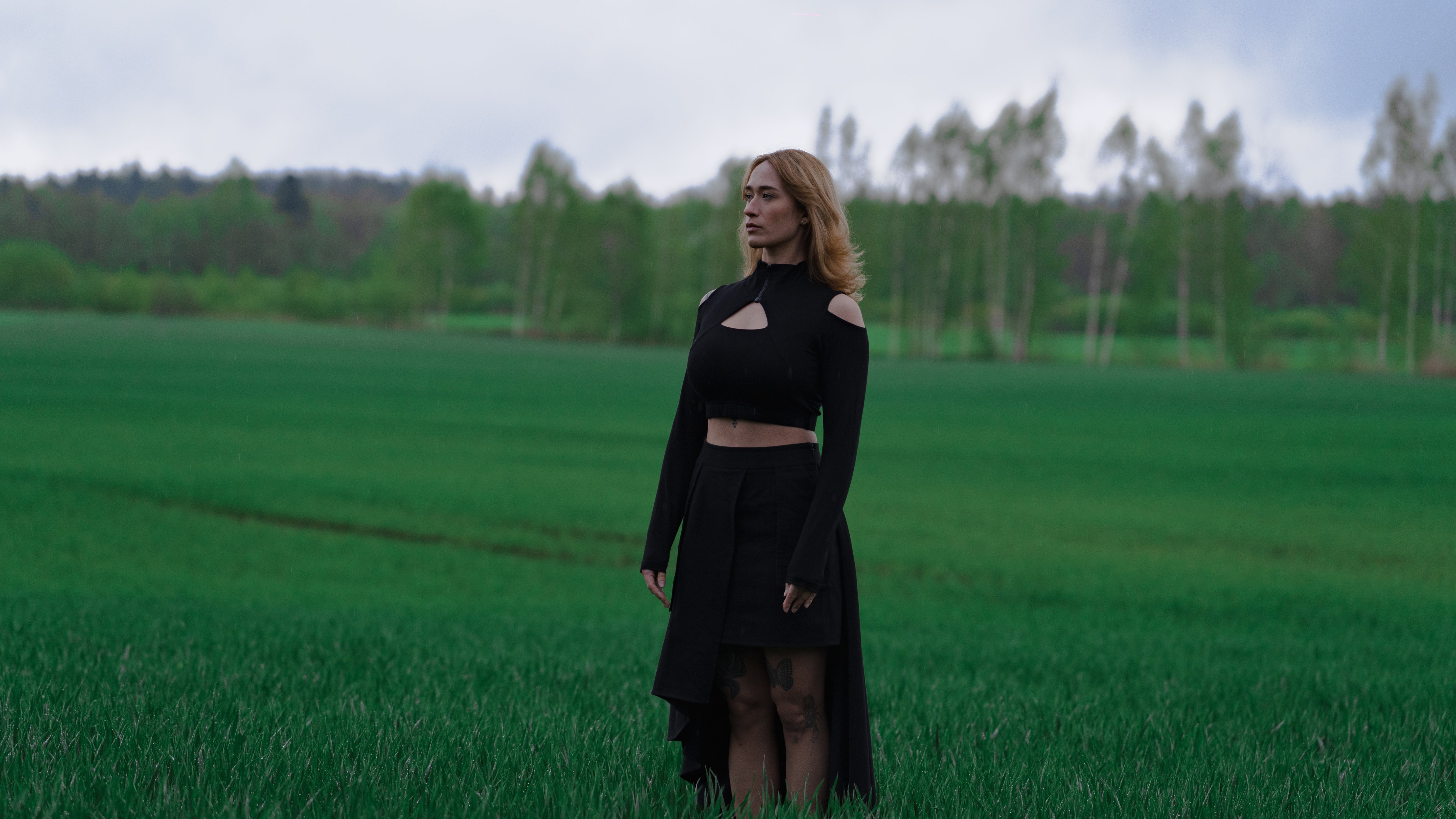 Woman in a black outfit standing in a green field with trees in the background