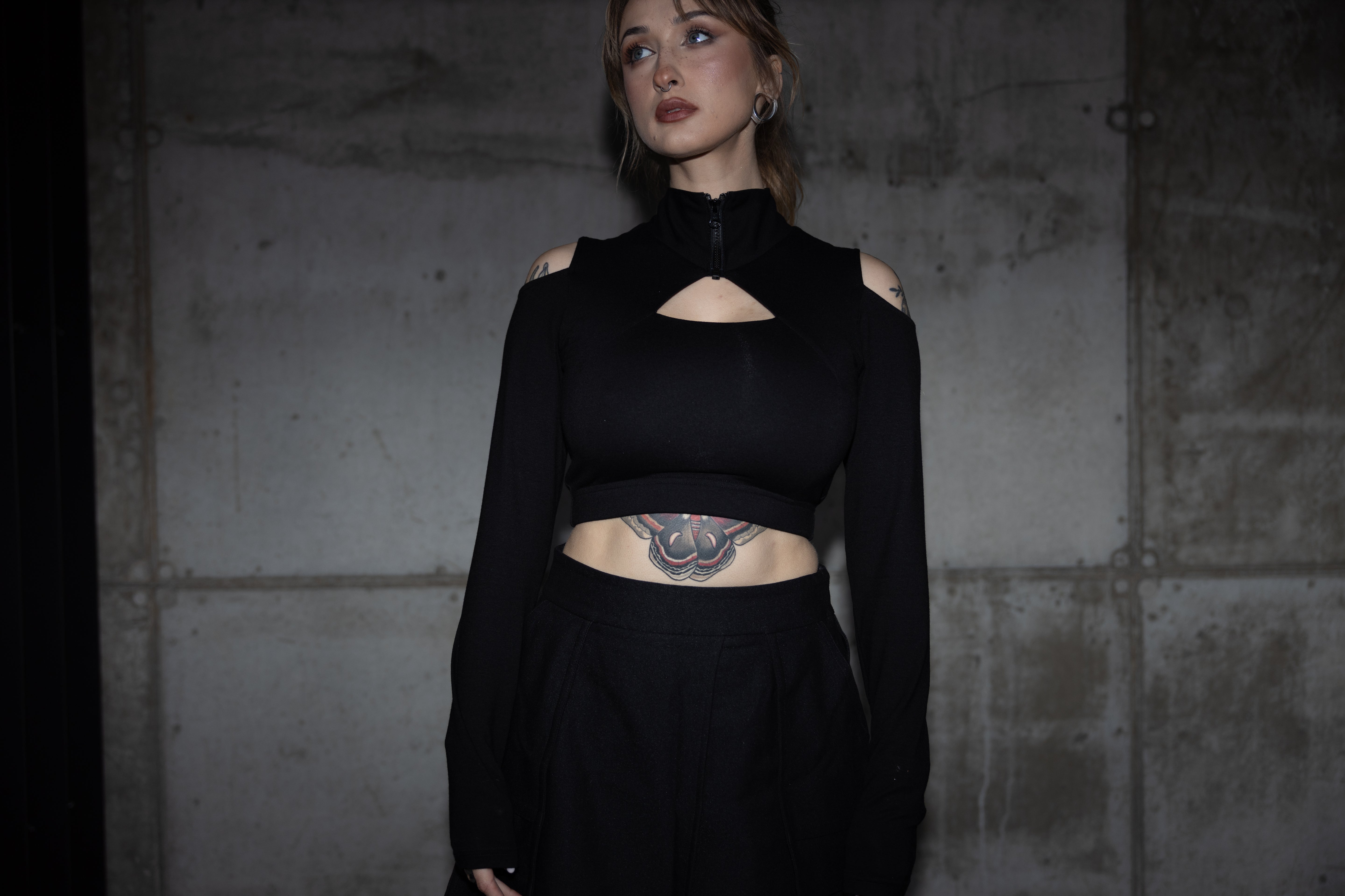 Person wearing a black outfit with cut-out design against a textured wall.