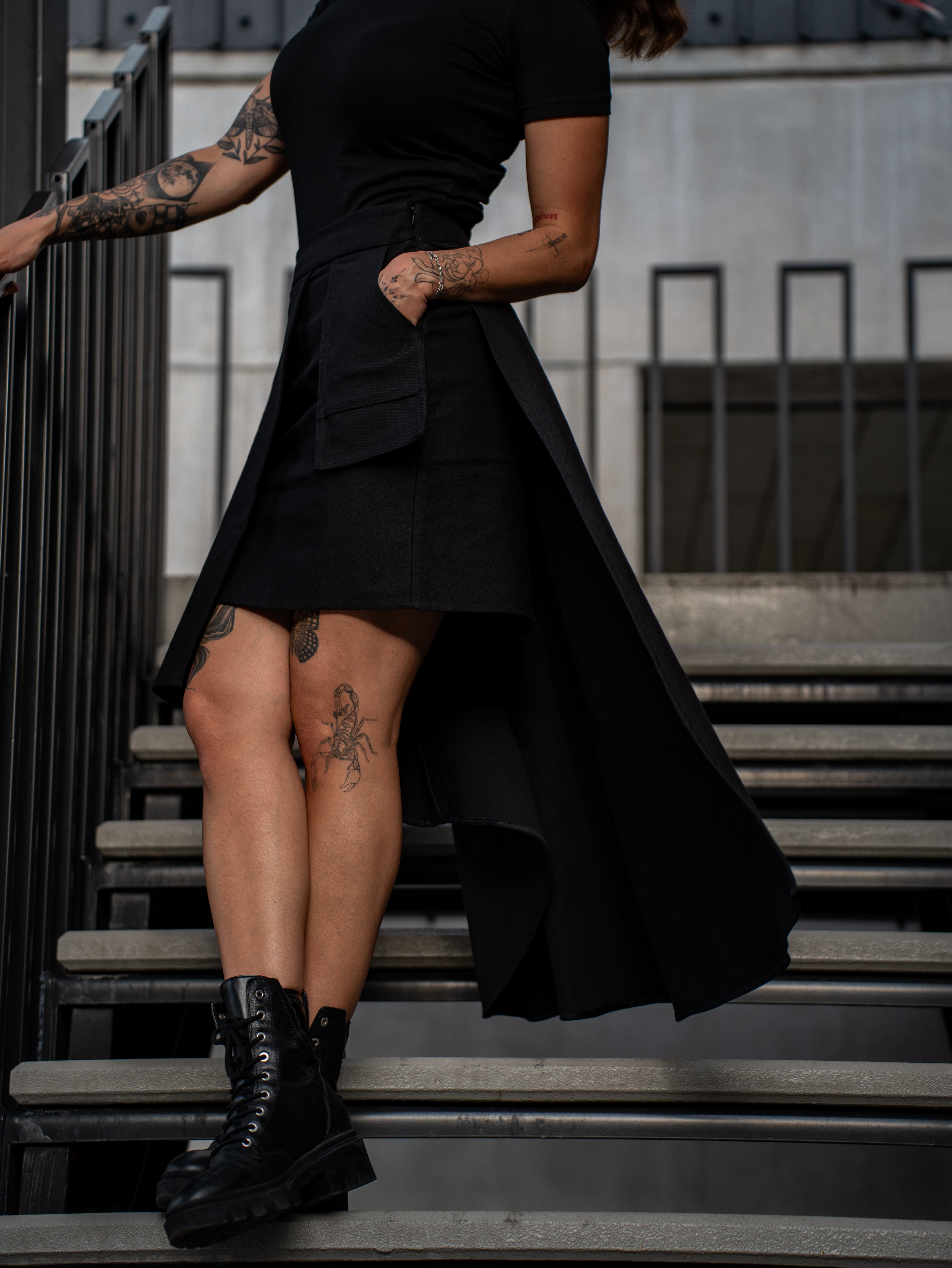 Person wearing a black dress and boots on steps with tattoos visible