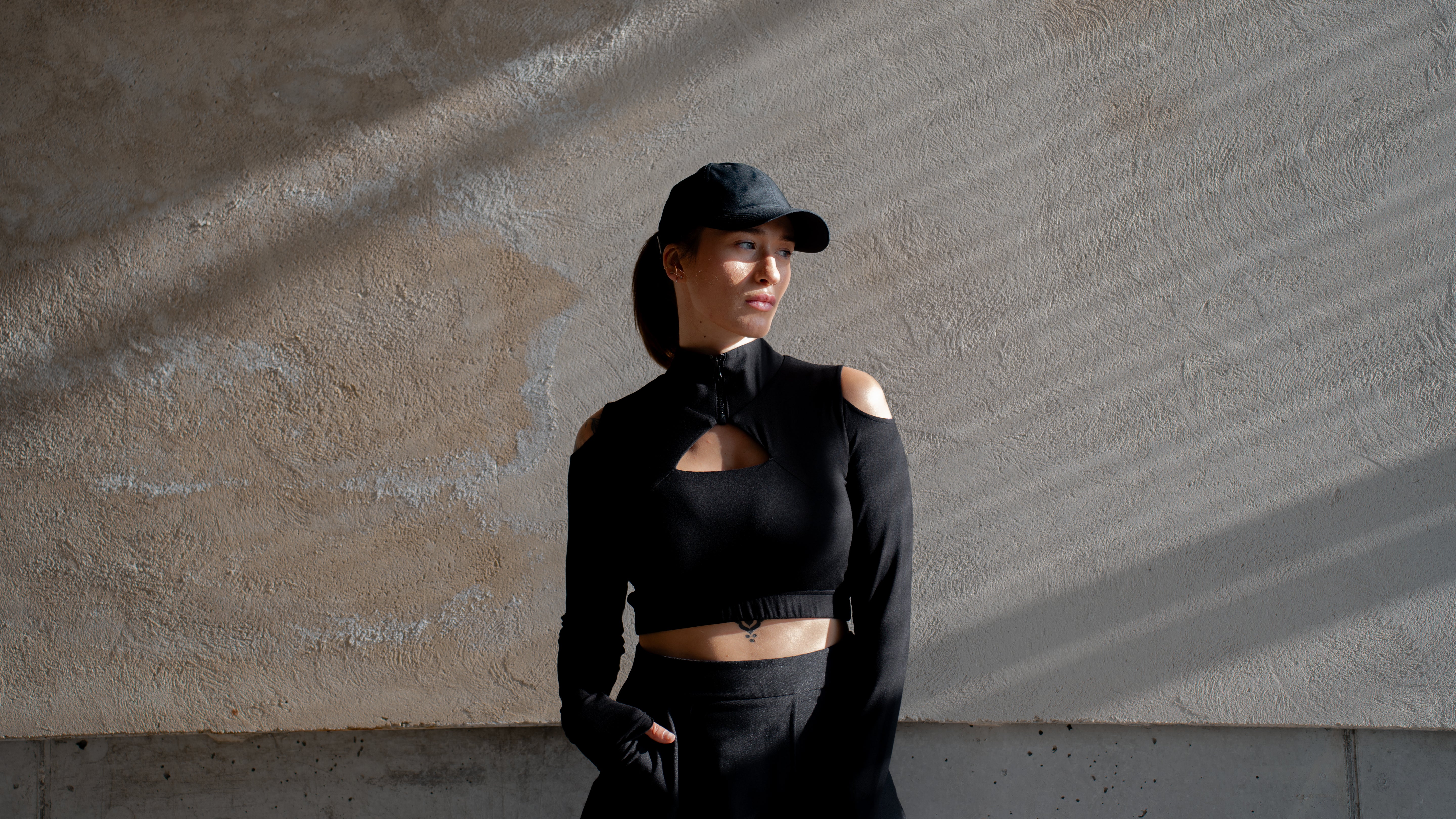 Person wearing a black outfit and cap against a textured wall