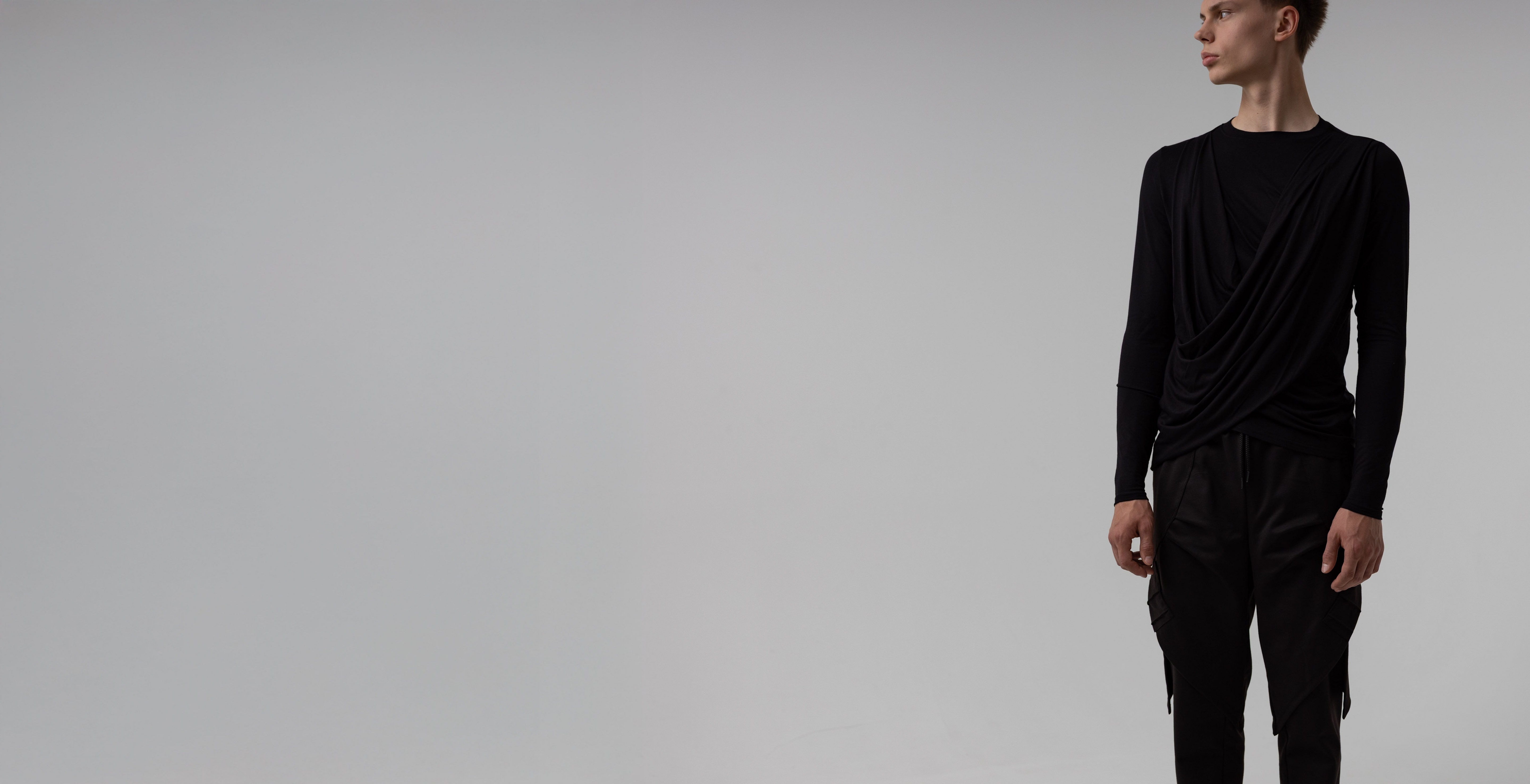 Male Person wearing a black fashion outfit with cargo pants and streetwear long sleeve shirt on a plain background