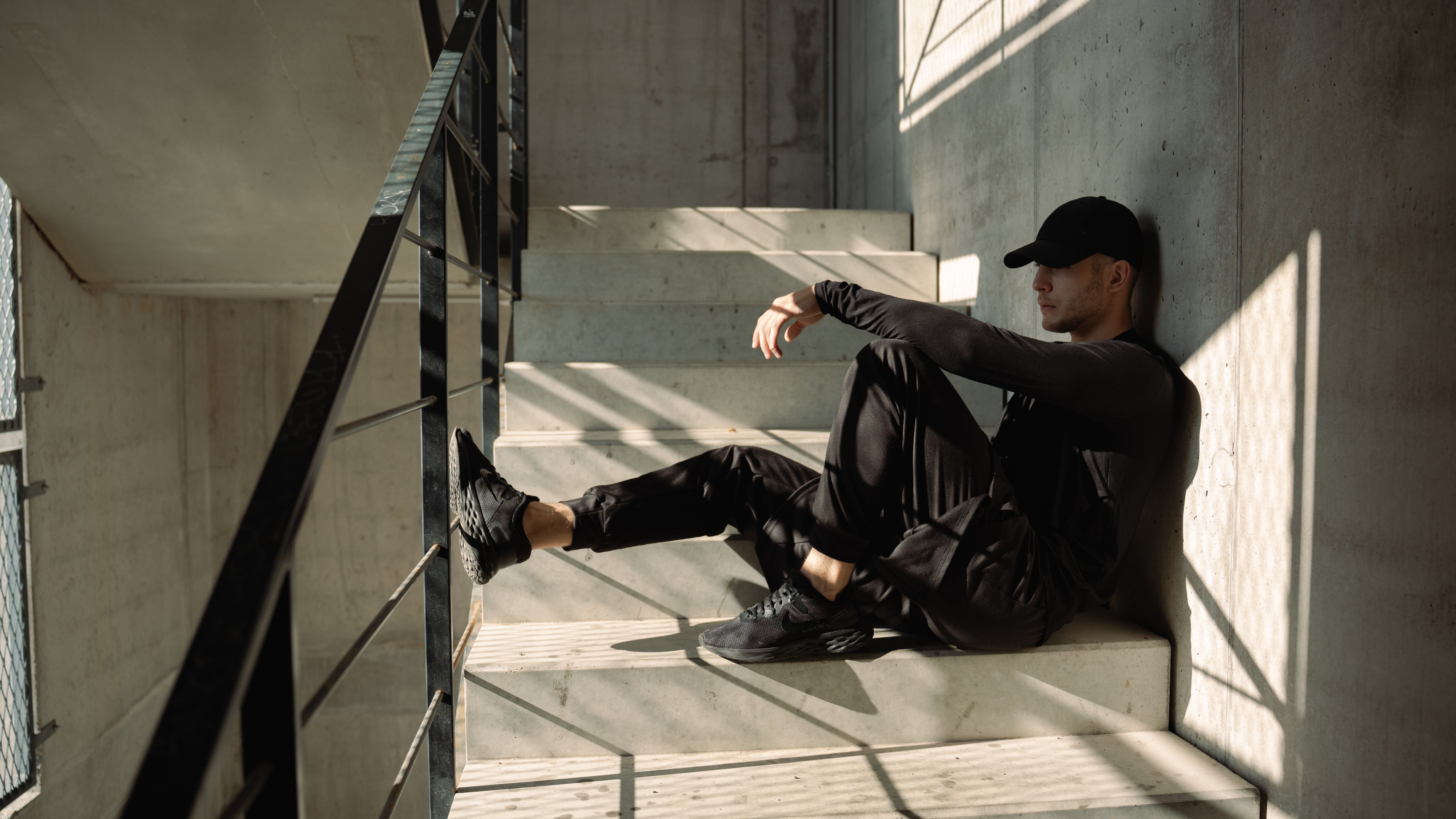 Person sitting on a staircase in an urban setting with all dark black new fashion trend of raw streetwear minimalism