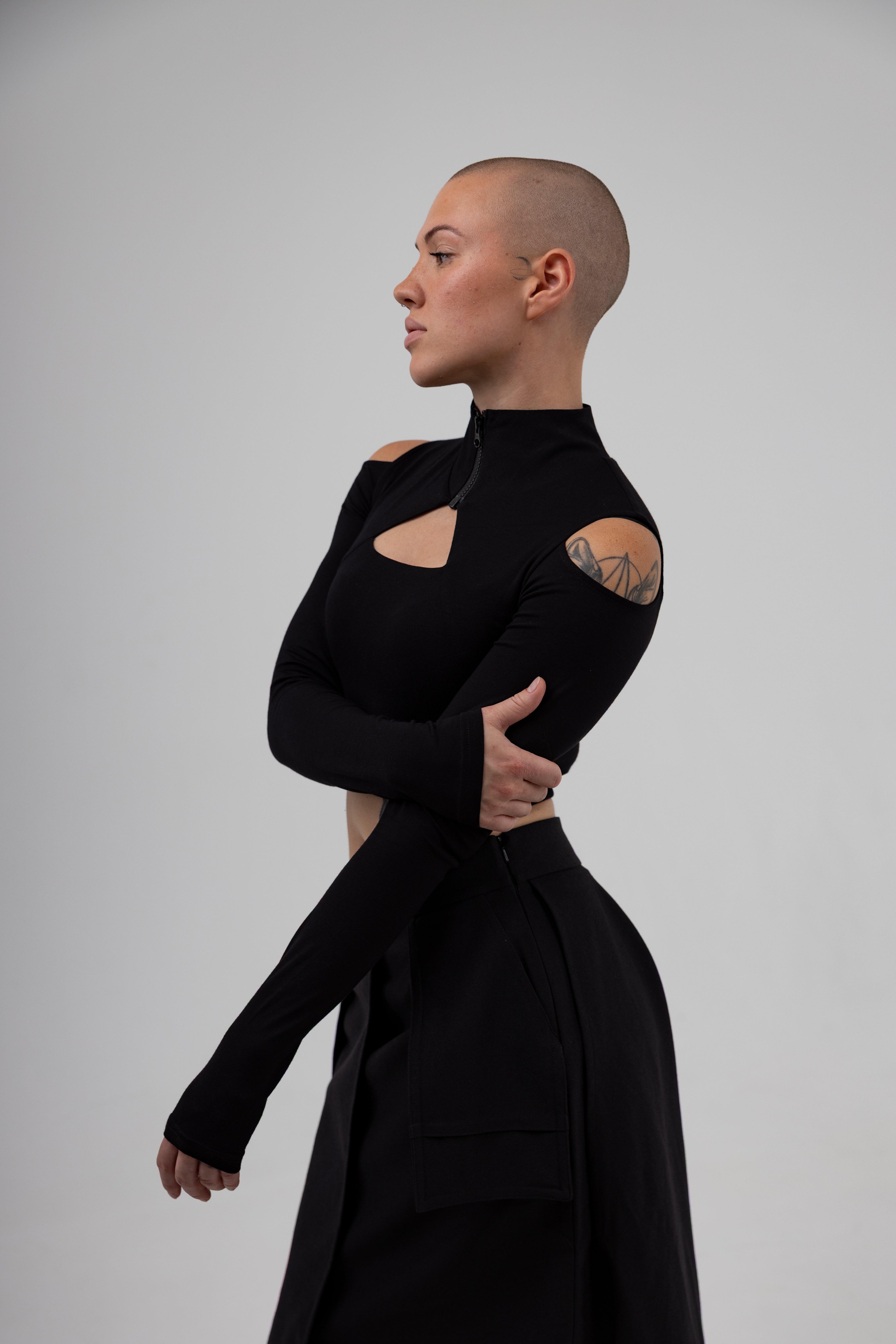 Person wearing a black outfit with cut-out design on a plain background